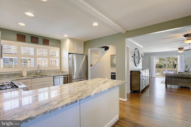 kitchen with open floor plan, light stone counters, appliances with stainless steel finishes, wood finished floors, and white cabinets