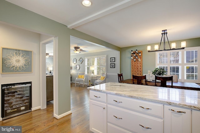 kitchen with light stone countertops, wine cooler, light wood-style floors, white cabinetry, and beamed ceiling