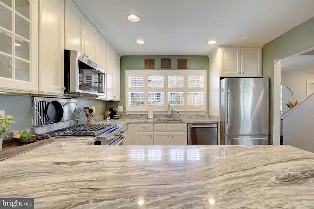 kitchen with glass insert cabinets, light stone counters, appliances with stainless steel finishes, white cabinetry, and a sink