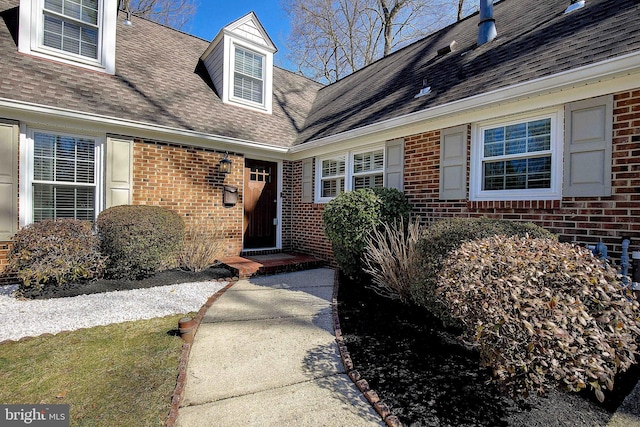 view of exterior entry with brick siding and roof with shingles