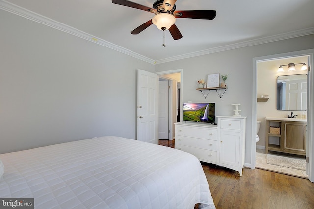 bedroom with crown molding, dark wood-type flooring, ensuite bathroom, a ceiling fan, and a sink