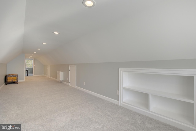 additional living space with vaulted ceiling, built in features, baseboards, and light carpet