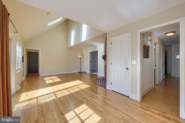 empty room featuring high vaulted ceiling, light wood-type flooring, and a skylight