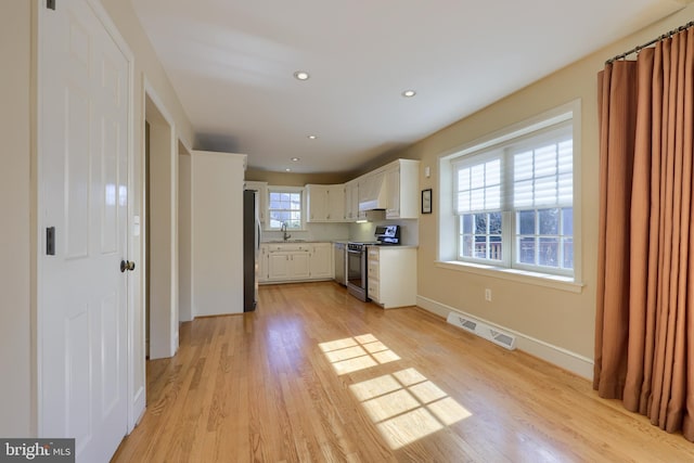 kitchen featuring light wood-type flooring, appliances with stainless steel finishes, white cabinetry, and sink