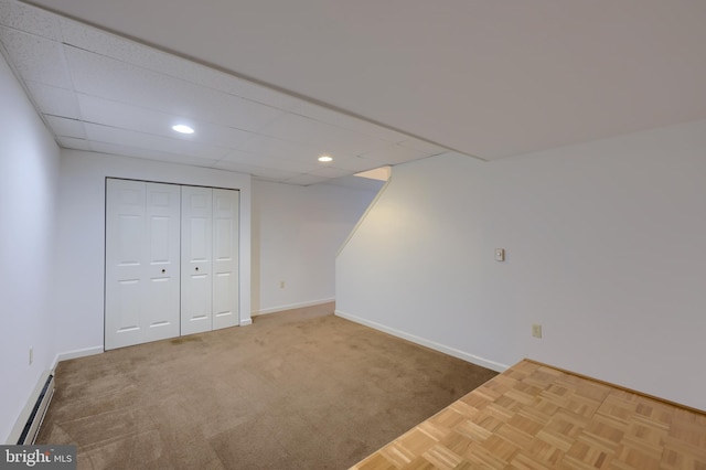 basement with a paneled ceiling, a baseboard heating unit, and carpet floors