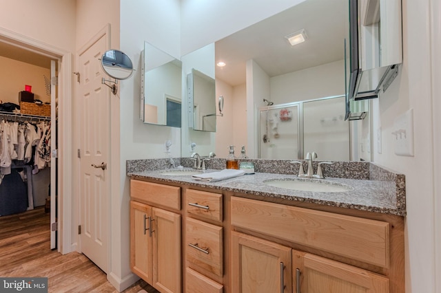 bathroom featuring a walk in closet, a shower stall, wood finished floors, and a sink