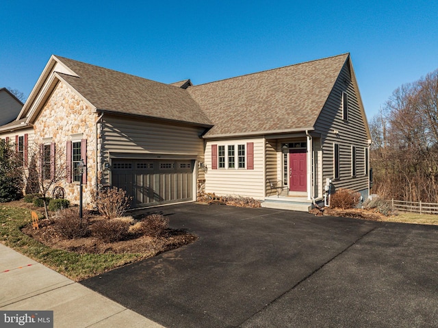 view of front of house featuring driveway, stone siding, fence, an attached garage, and a shingled roof