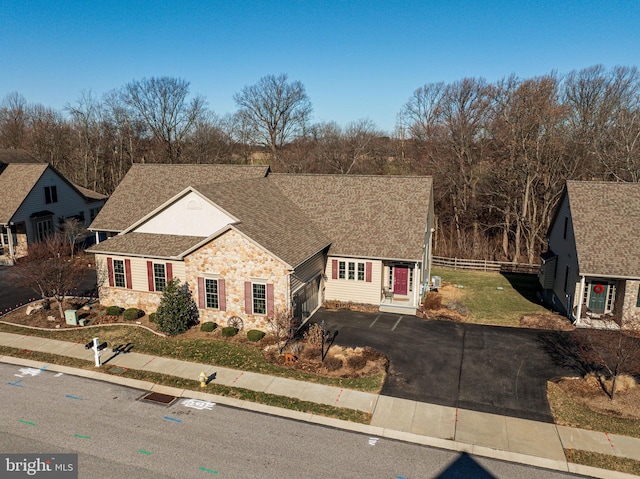 view of front of home featuring a front yard, fence, driveway, a shingled roof, and stone siding