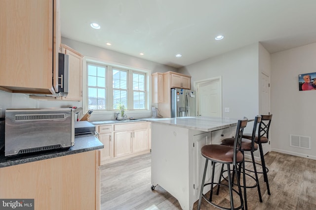 kitchen featuring a kitchen bar, visible vents, light brown cabinetry, a kitchen island, and stainless steel appliances