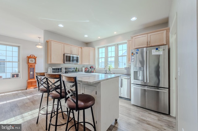 kitchen with light wood-type flooring, a kitchen breakfast bar, appliances with stainless steel finishes, and light brown cabinets