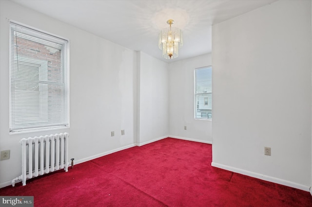 spare room featuring carpet, radiator, and a notable chandelier