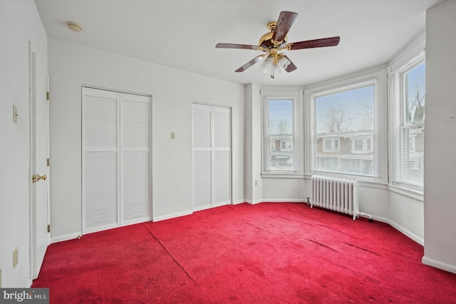 unfurnished bedroom featuring radiator, carpet floors, multiple closets, and ceiling fan