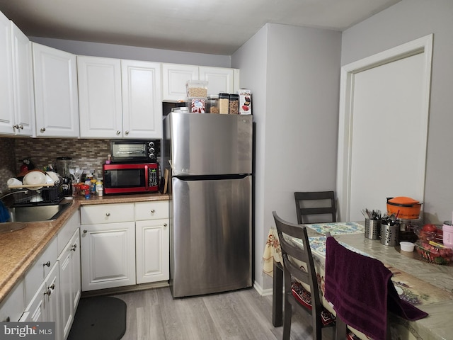 kitchen with sink, white cabinets, stainless steel refrigerator, and light hardwood / wood-style floors