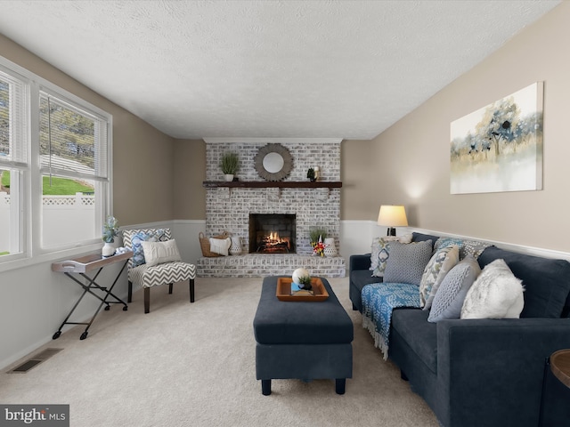 living area featuring light colored carpet, visible vents, a brick fireplace, wainscoting, and a textured ceiling