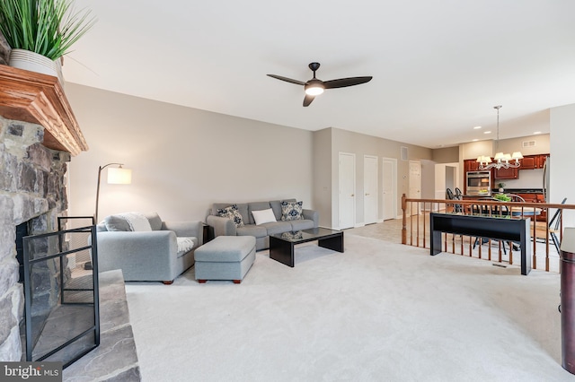 living room featuring light colored carpet, a stone fireplace, and ceiling fan with notable chandelier