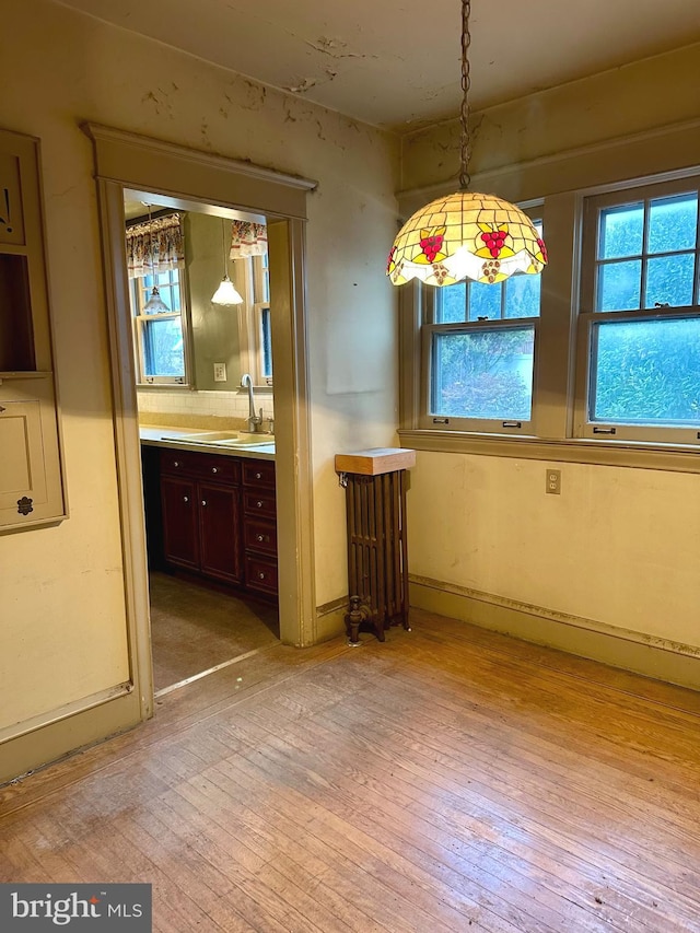 unfurnished dining area featuring sink, light hardwood / wood-style flooring, and radiator heating unit