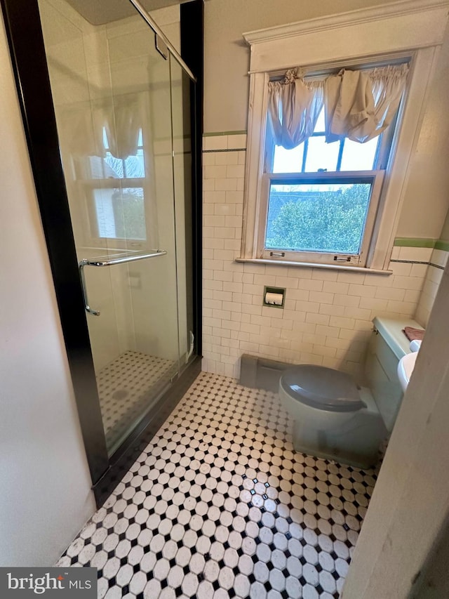 bathroom featuring tile patterned flooring, toilet, tile walls, and a shower with shower door