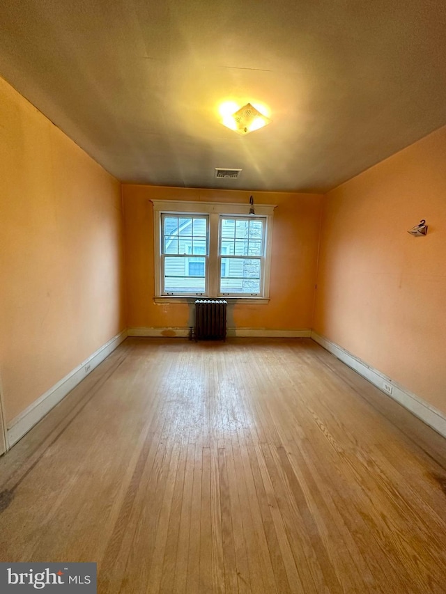 spare room featuring radiator heating unit and light hardwood / wood-style floors