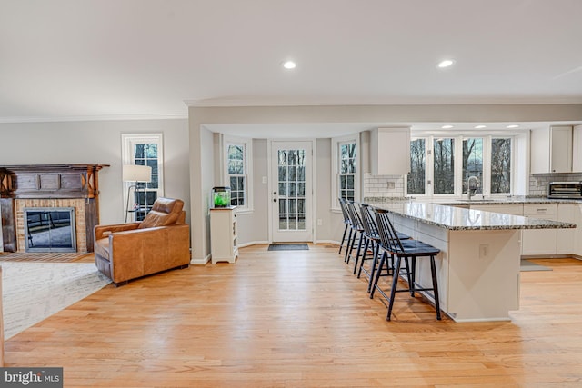 kitchen featuring white cabinetry, light stone counters, tasteful backsplash, a kitchen bar, and a brick fireplace