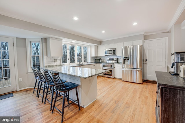 kitchen with light hardwood / wood-style flooring, a breakfast bar area, stainless steel appliances, white cabinets, and kitchen peninsula