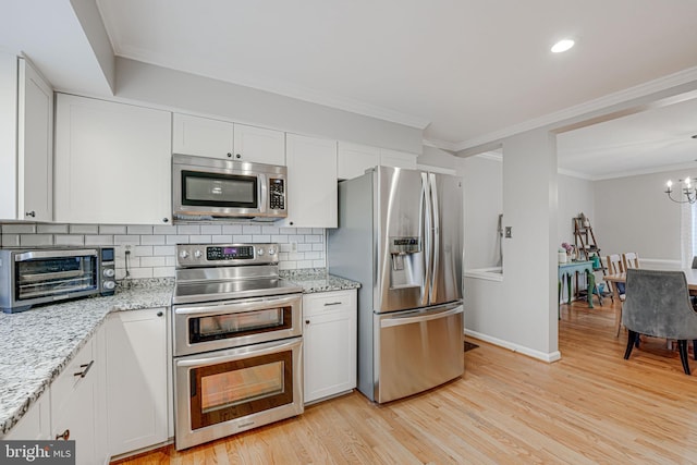 kitchen with appliances with stainless steel finishes, white cabinets, decorative backsplash, light stone counters, and light wood-type flooring