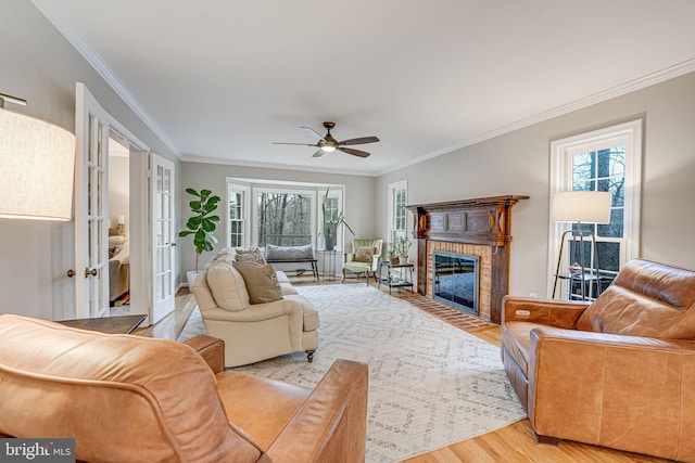 living room with a fireplace, ornamental molding, ceiling fan, and light wood-type flooring