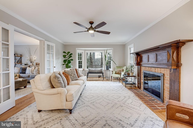 living room featuring a brick fireplace, crown molding, wood-type flooring, and ceiling fan