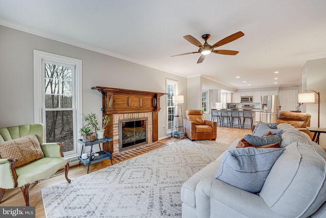 living room with ornamental molding, plenty of natural light, a brick fireplace, and light hardwood / wood-style flooring