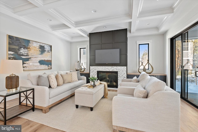 living room featuring beamed ceiling, coffered ceiling, a tiled fireplace, and light wood-type flooring