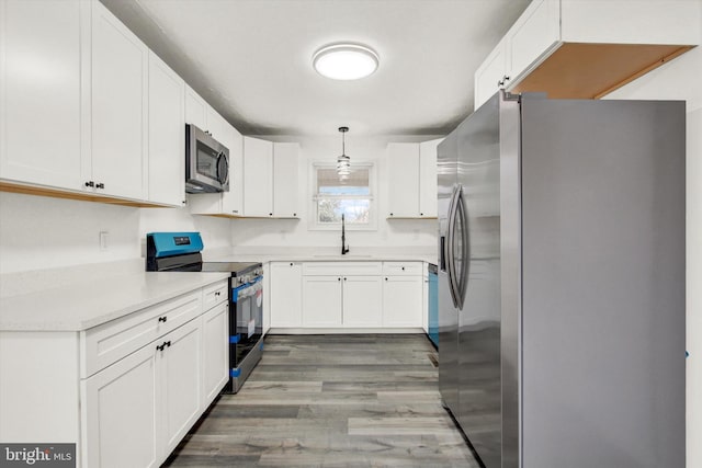 kitchen with white cabinetry, stainless steel appliances, sink, and hanging light fixtures