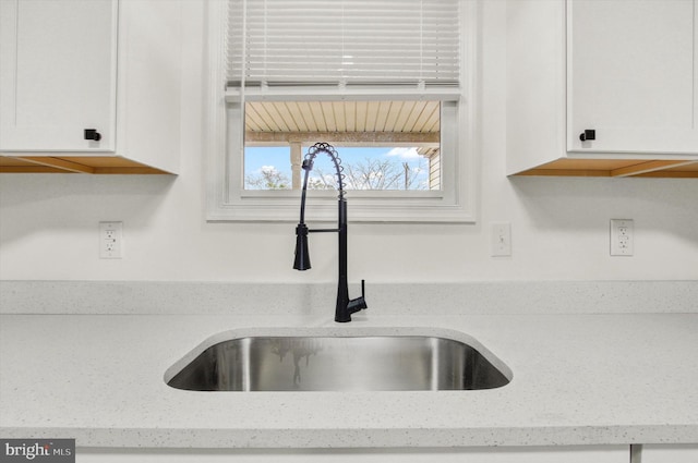 room details with light stone counters, sink, and white cabinets