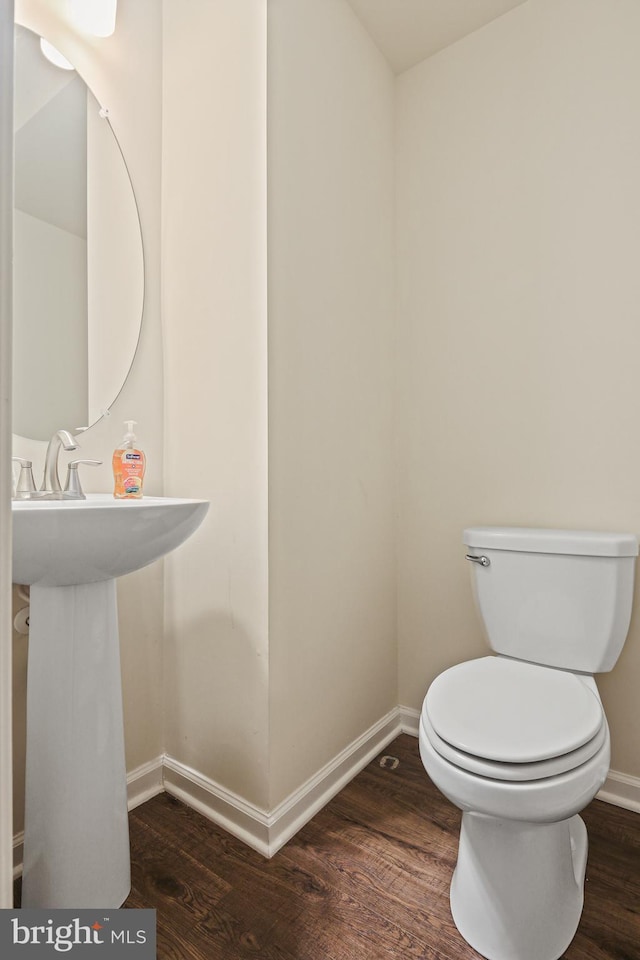 half bath featuring wood finished floors, toilet, and baseboards