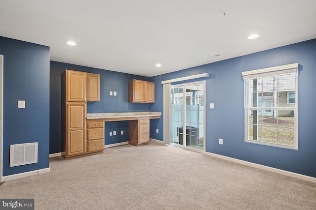 interior space with light carpet, baseboards, visible vents, light countertops, and built in desk