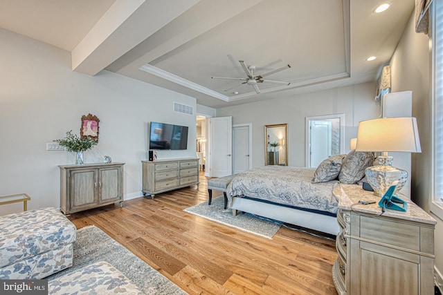 bedroom with ceiling fan, light wood-type flooring, and a tray ceiling