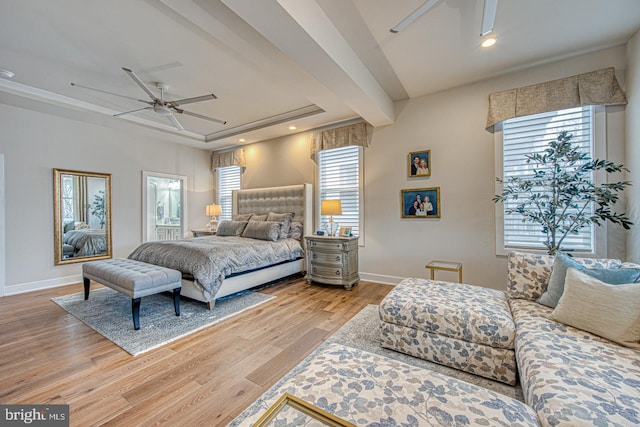 bedroom with ceiling fan, connected bathroom, light hardwood / wood-style floors, and a tray ceiling