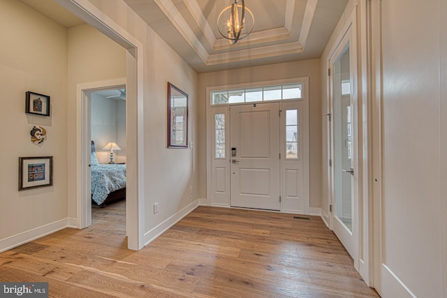 entrance foyer featuring a raised ceiling, crown molding, a chandelier, and light hardwood / wood-style flooring