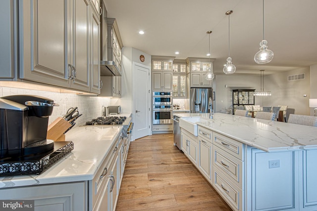 kitchen with appliances with stainless steel finishes, pendant lighting, a spacious island, sink, and light hardwood / wood-style flooring