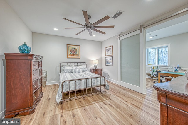 bedroom with ceiling fan, a barn door, and light hardwood / wood-style flooring