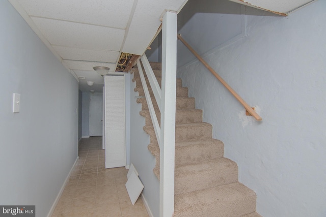 staircase with a paneled ceiling and tile patterned floors