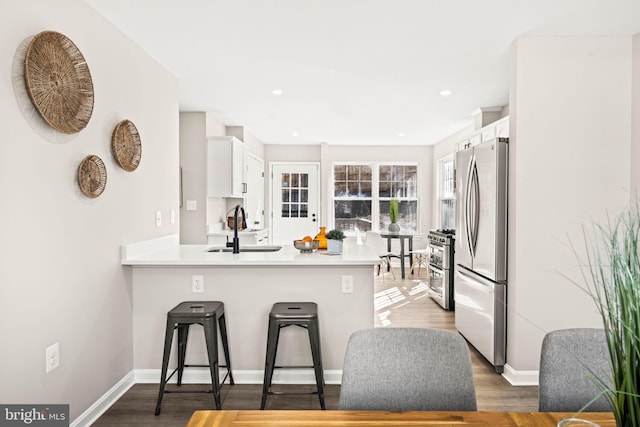 kitchen featuring kitchen peninsula, stainless steel appliances, sink, white cabinets, and a kitchen bar