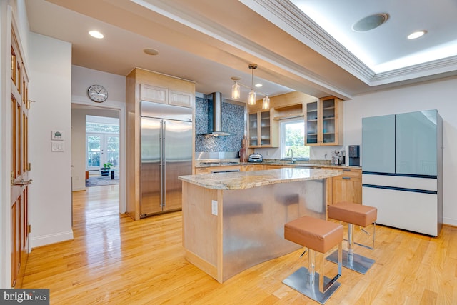 kitchen with wall chimney range hood, appliances with stainless steel finishes, a kitchen island, and glass insert cabinets