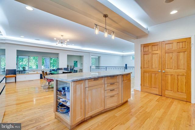 kitchen featuring a kitchen island, open floor plan, hanging light fixtures, light stone countertops, and light brown cabinets