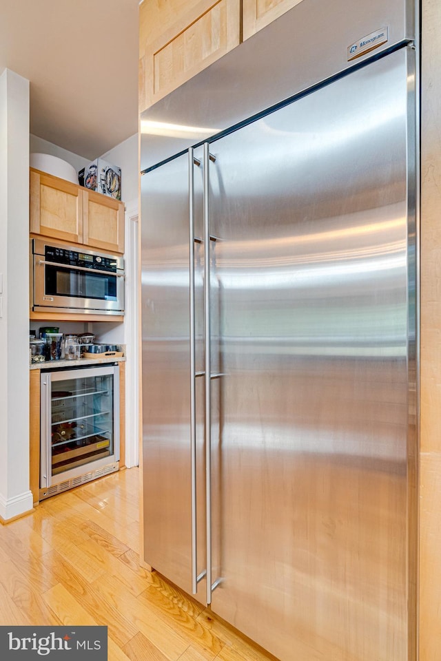 kitchen with stainless steel appliances, light countertops, light wood-style flooring, light brown cabinetry, and beverage cooler