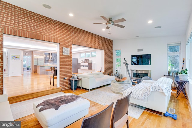 living room with recessed lighting, brick wall, a fireplace, visible vents, and light wood-style floors