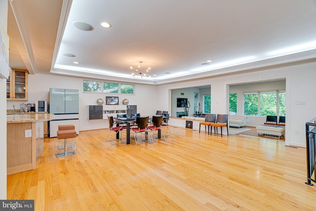 dining area featuring an inviting chandelier, a tray ceiling, light wood finished floors, and recessed lighting