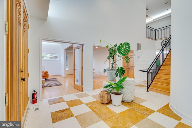 foyer entrance with a towering ceiling, stairway, baseboards, and visible vents