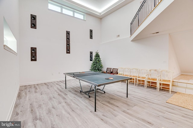 recreation room featuring light wood-type flooring, visible vents, a towering ceiling, and baseboards