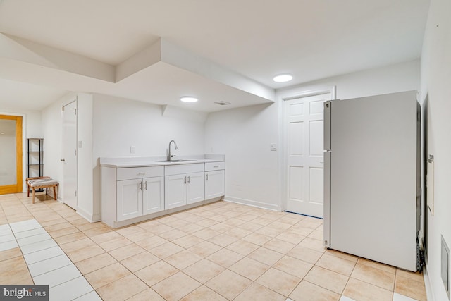 kitchen with light tile patterned floors, light countertops, freestanding refrigerator, white cabinets, and a sink