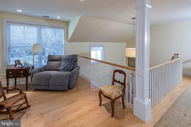 living area with wood finished floors, an upstairs landing, visible vents, vaulted ceiling, and ornate columns