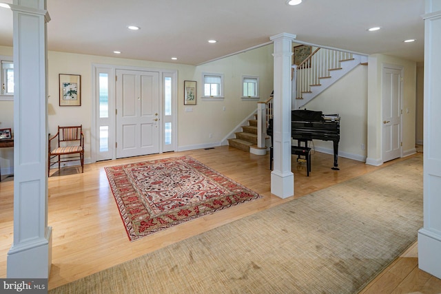 foyer featuring a wealth of natural light, light wood-style flooring, stairway, and decorative columns